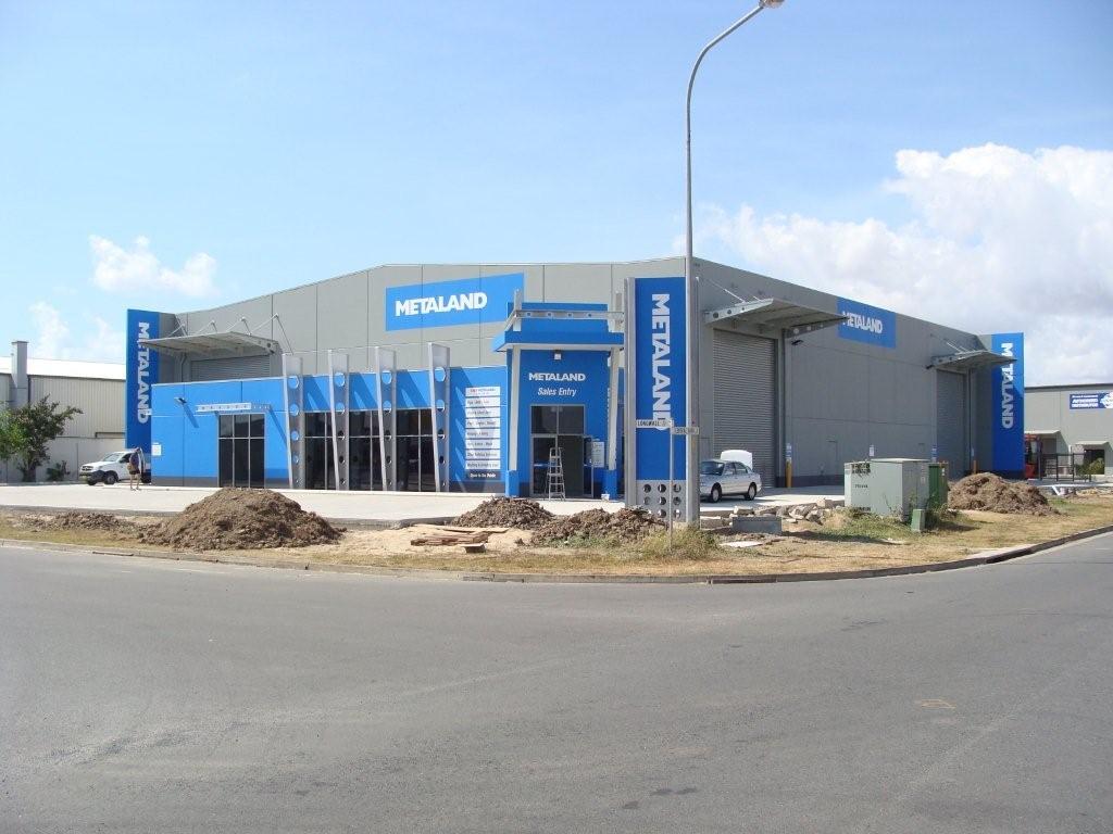 Blue and gray Hedland store with signage on a corner lot under a blue sky.