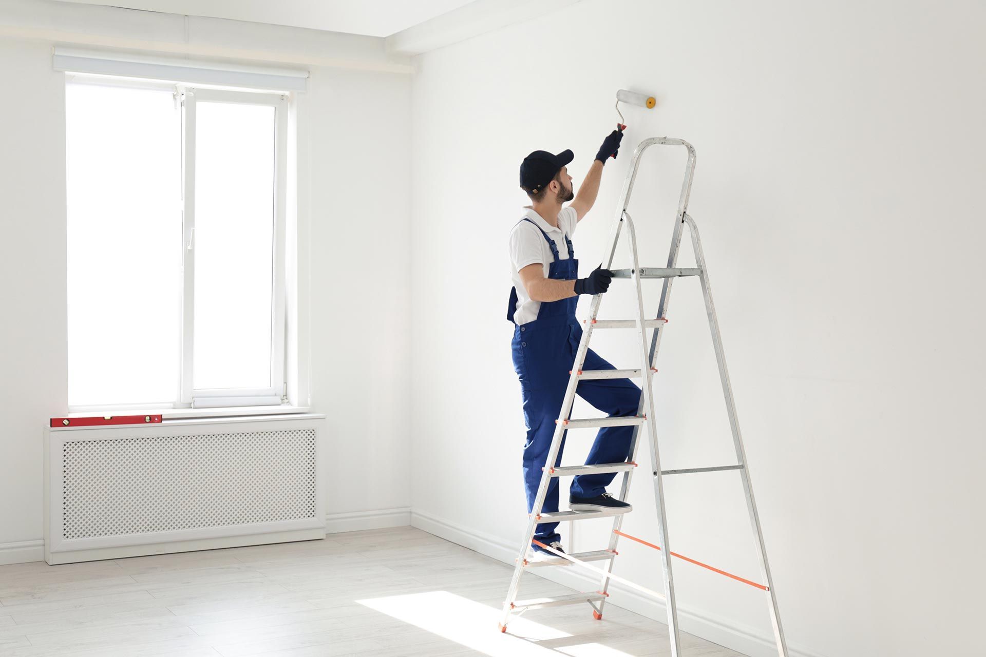 A residential painter is painting a white wall with a roller brush. A residential painter is painting a white wall with a roller brush.