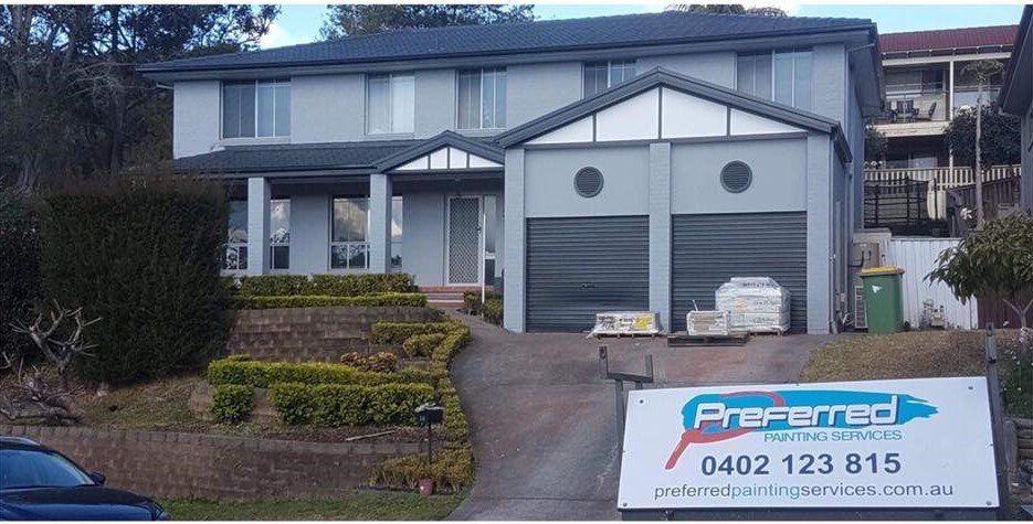 Two-story gray house with a driveway and a sign advertising painting services.