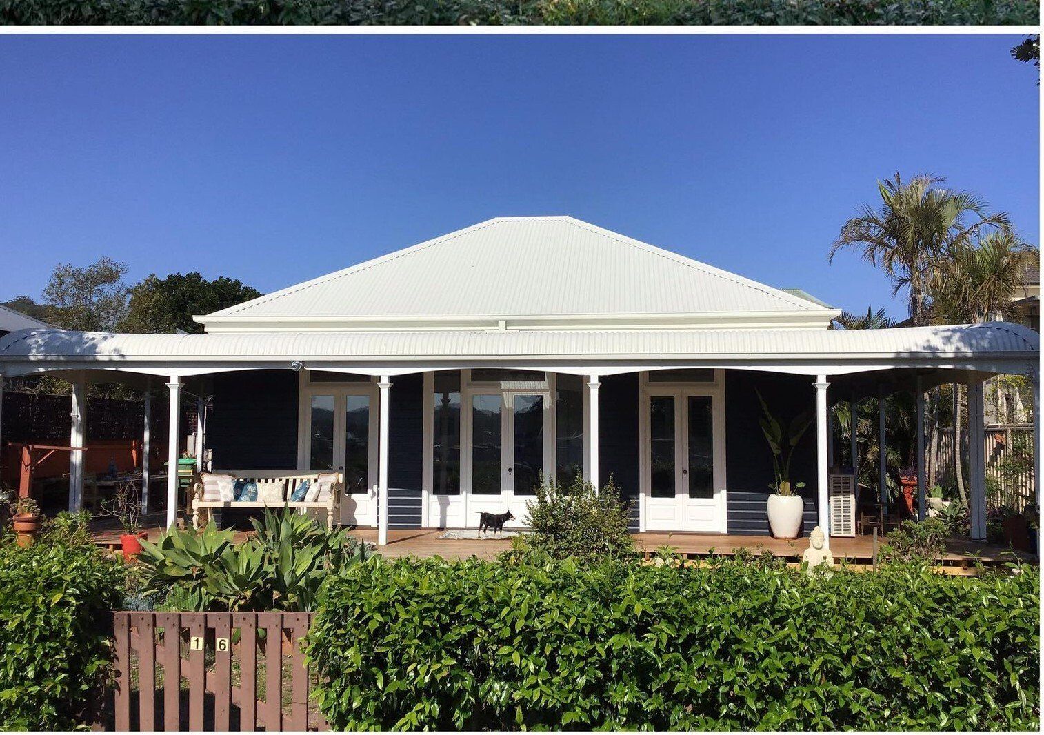 A blue house with white trim, a white roof, and a wraparound porch, on a sunny day.