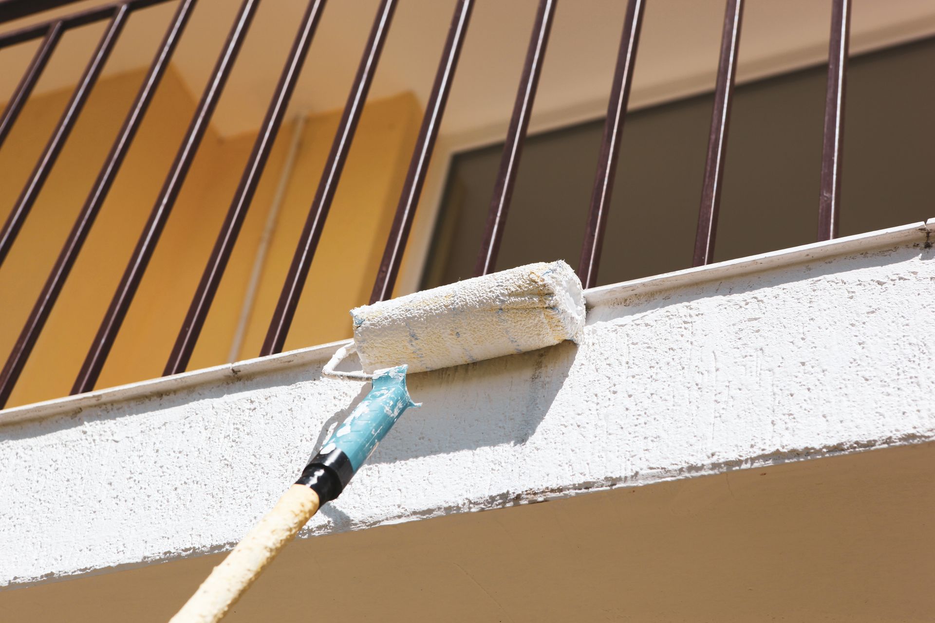 Paint roller painting a white textured balcony ledge.