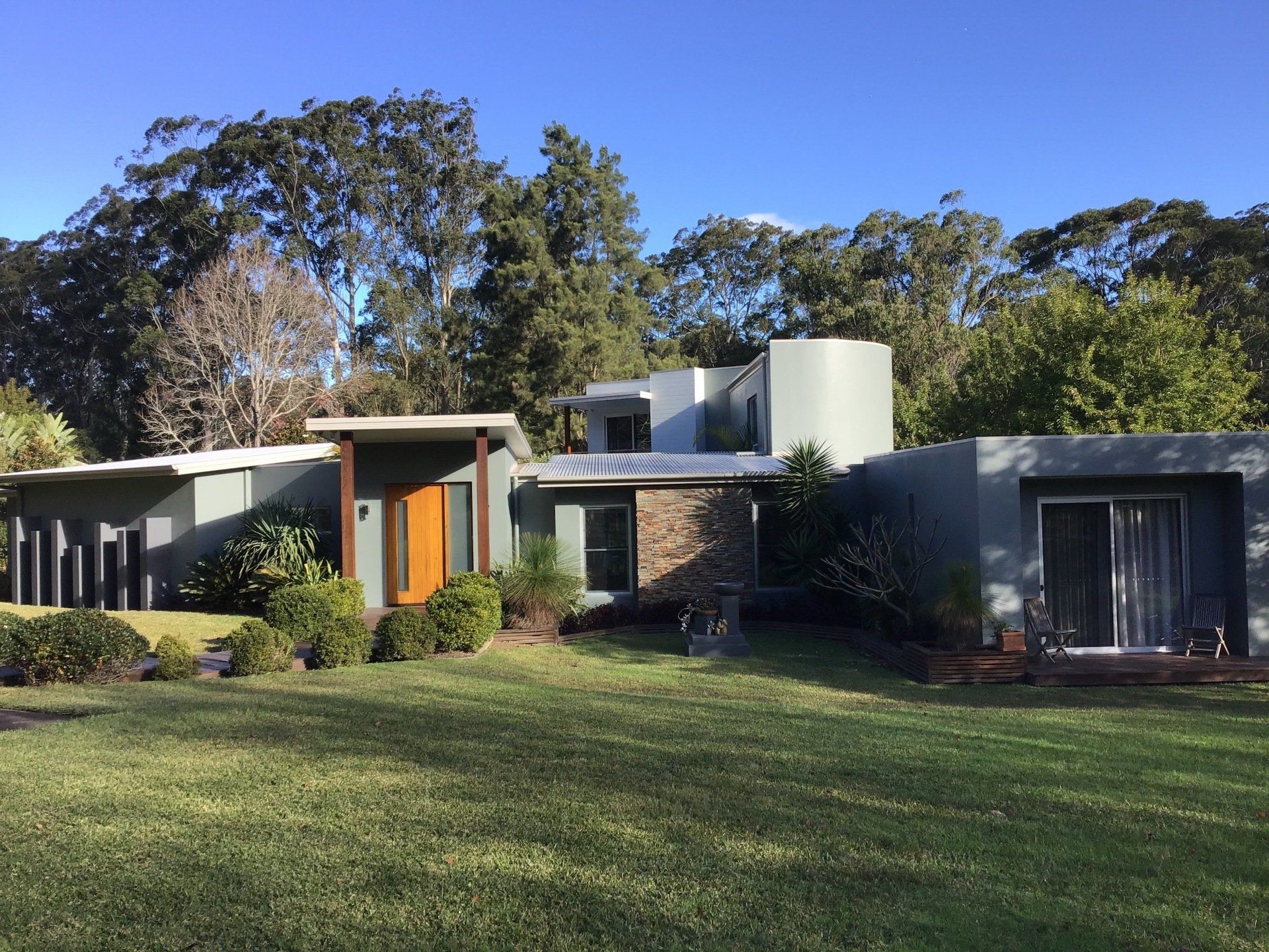 Modern house with gray exterior, wooden door, and surrounding trees.