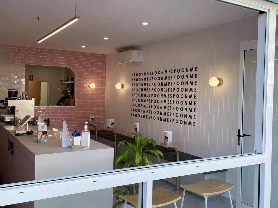 A small cafe interior with a white counter, pink tiled wall, and a large word art piece.