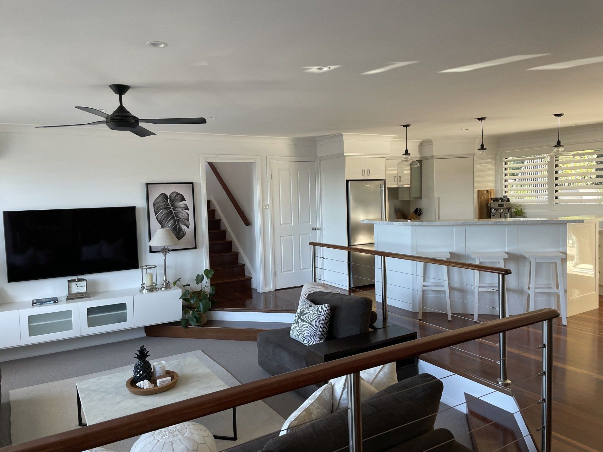 Living room with white walls, TV, stairs, kitchen bar, and brown wooden floors.