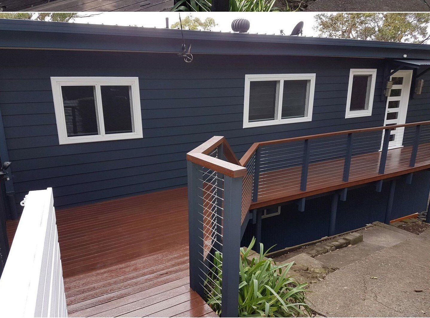 Dark blue house with a brown deck and white window frames.