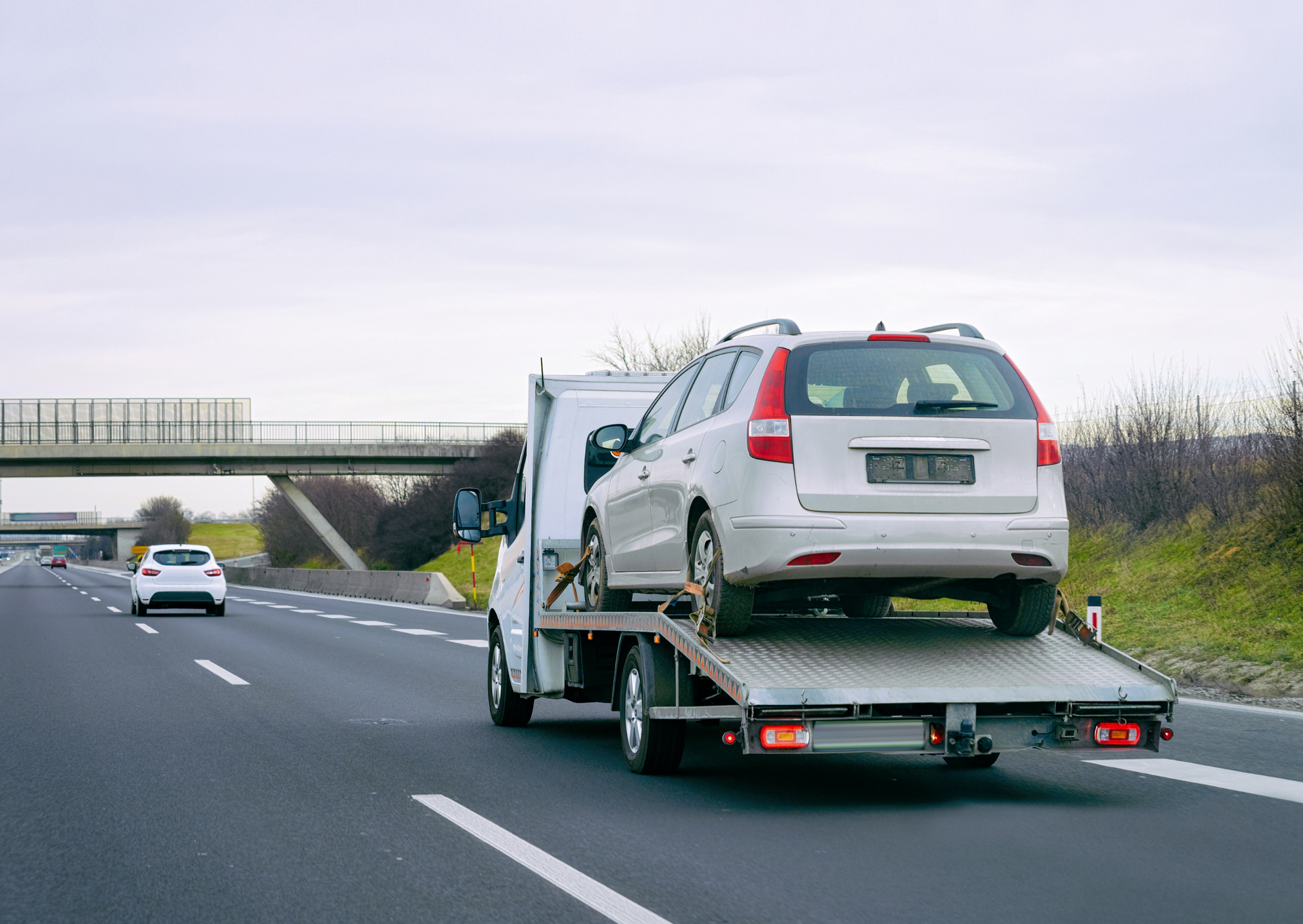 A tow truck is towing a white car on a highway.
