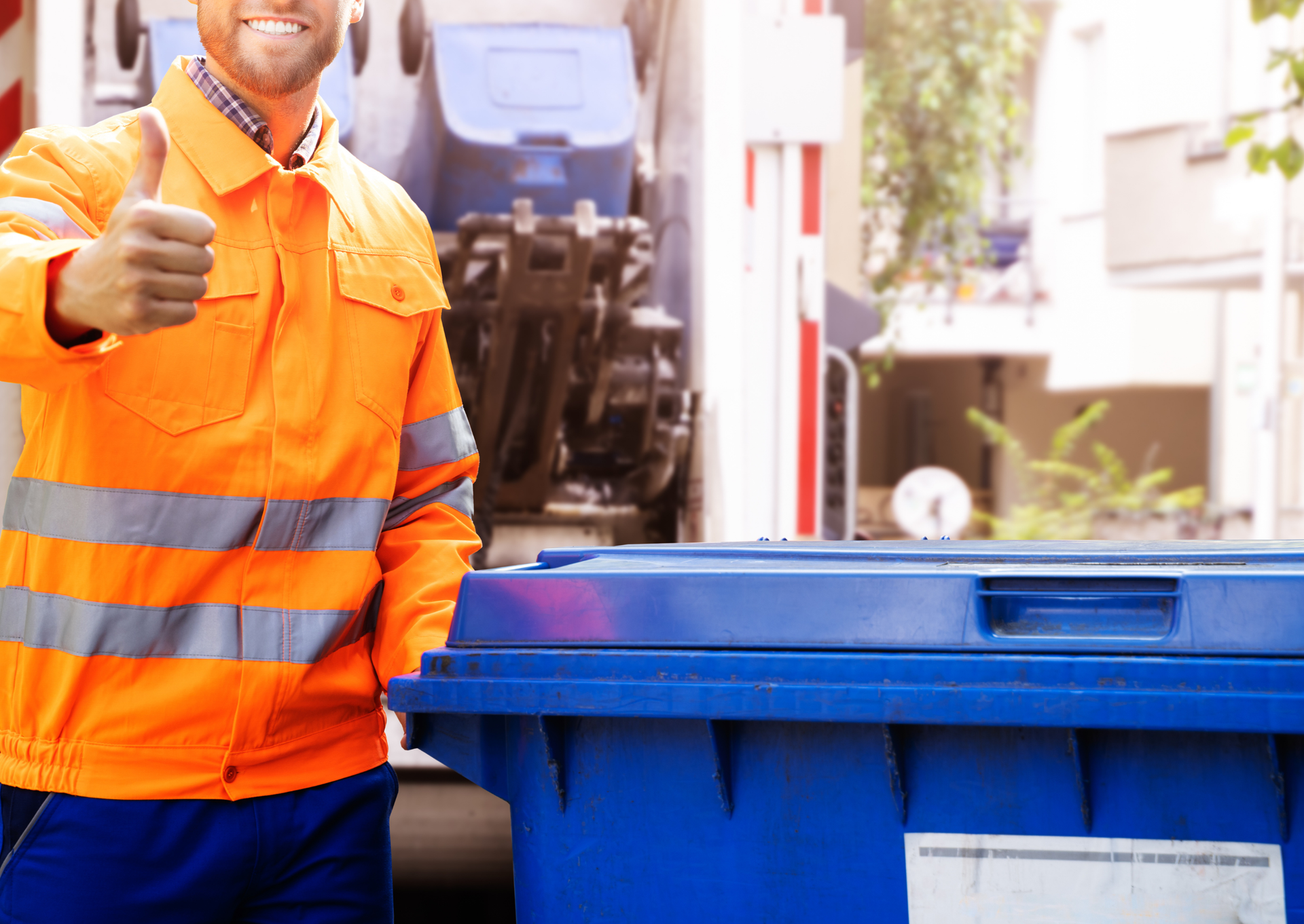 A man is giving a thumbs up while standing next to a blue trash can.