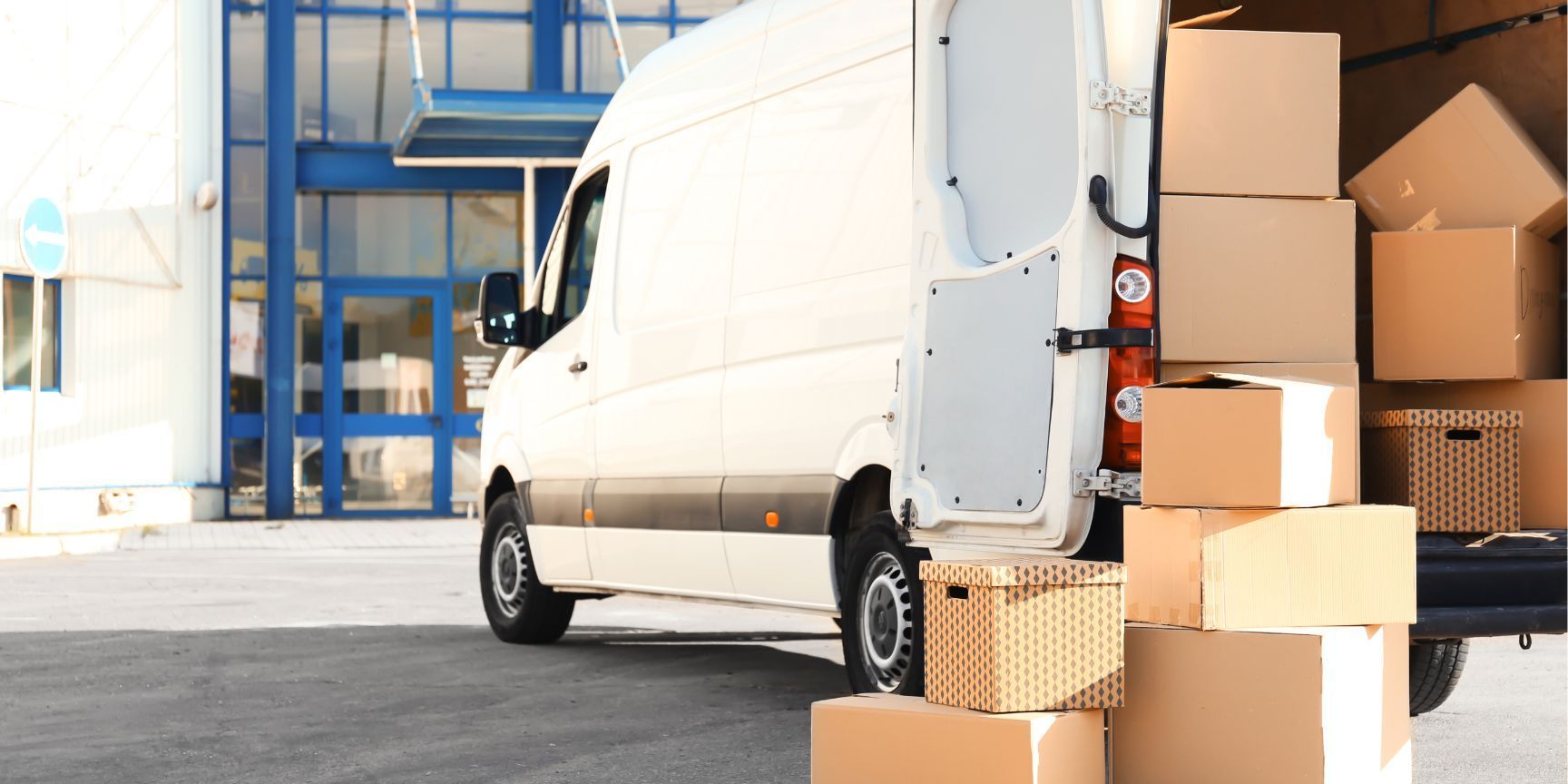 A white delivery van is loaded with boxes in front of a building.