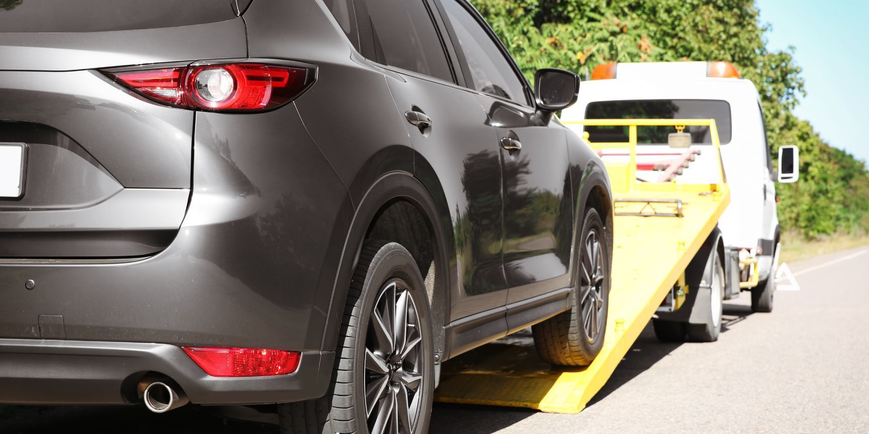 A car is being towed by a tow truck on the side of the road.