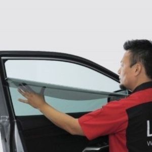 A man is applying window tinting to a car door window.