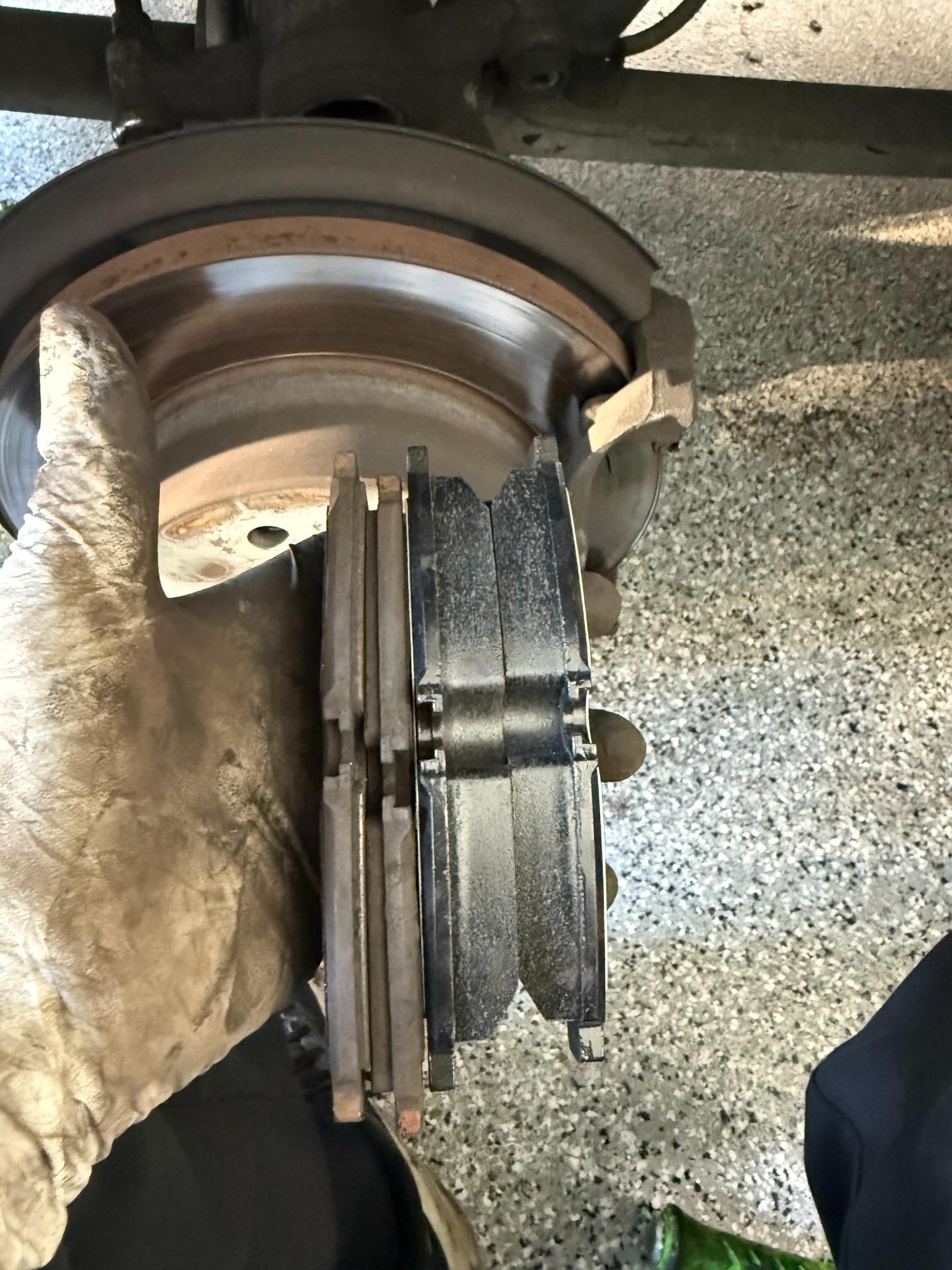 Close-up of worn brake pads next to a brake rotor on a vehicle, showing wear and comparison.