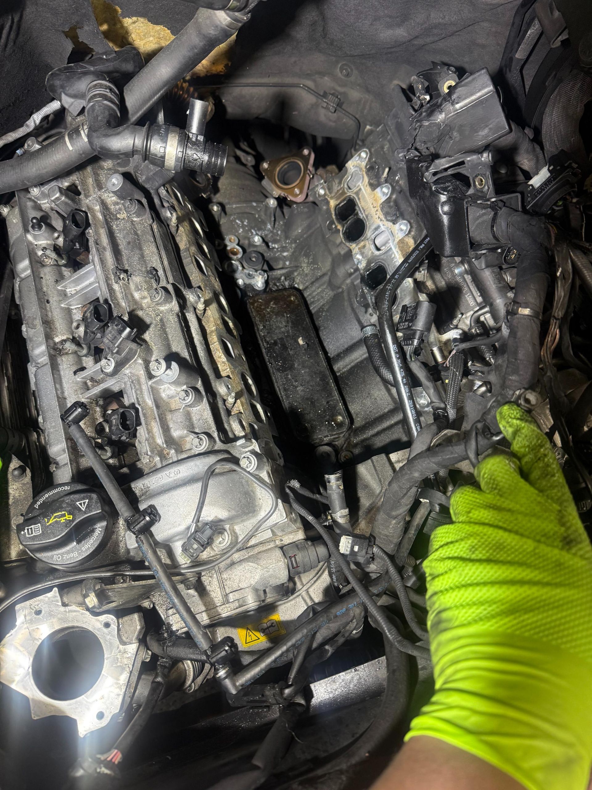 fleet vehicle engine heavily damaged by fire. A hand in a yellow glove examines the charred remains.