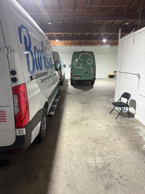 Three fleet vans parked inside a garage; one white, one green, one partially visible. A black chair sits nearby.