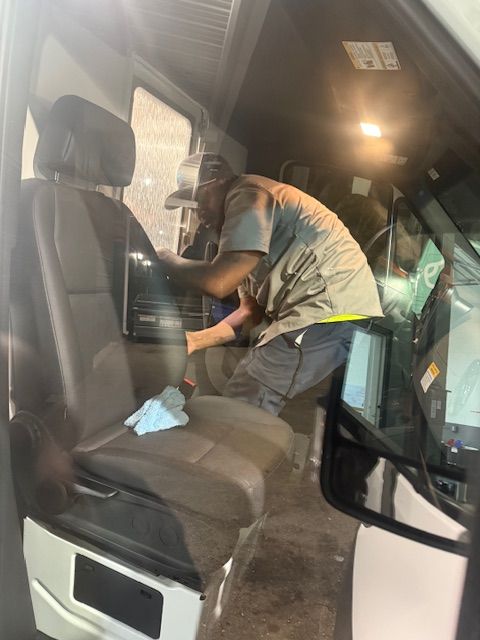 Man working on interior of a fleet vehicle; dark interior with a driver's seat.