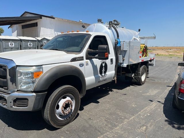 White fleet truck with a large tank parked near portable toilets.