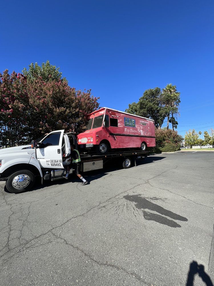 Tow truck hauling a red food truck on a sunny day.