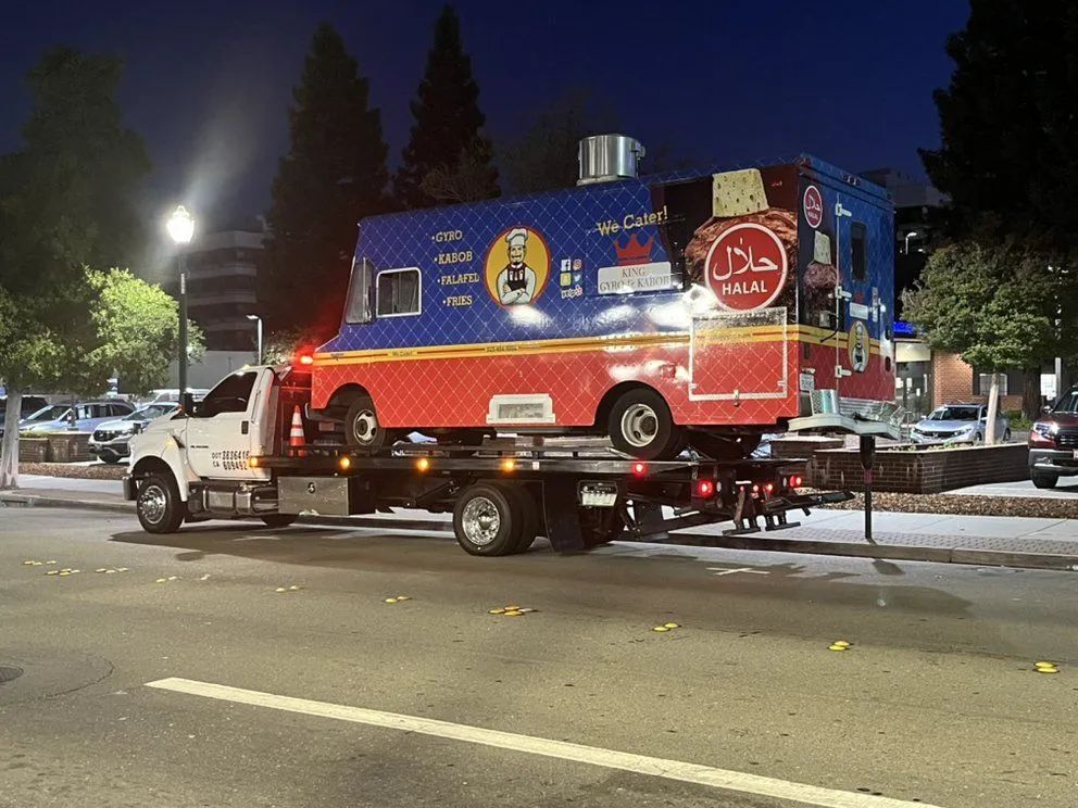 Food truck being towed on a flatbed truck at night, with 