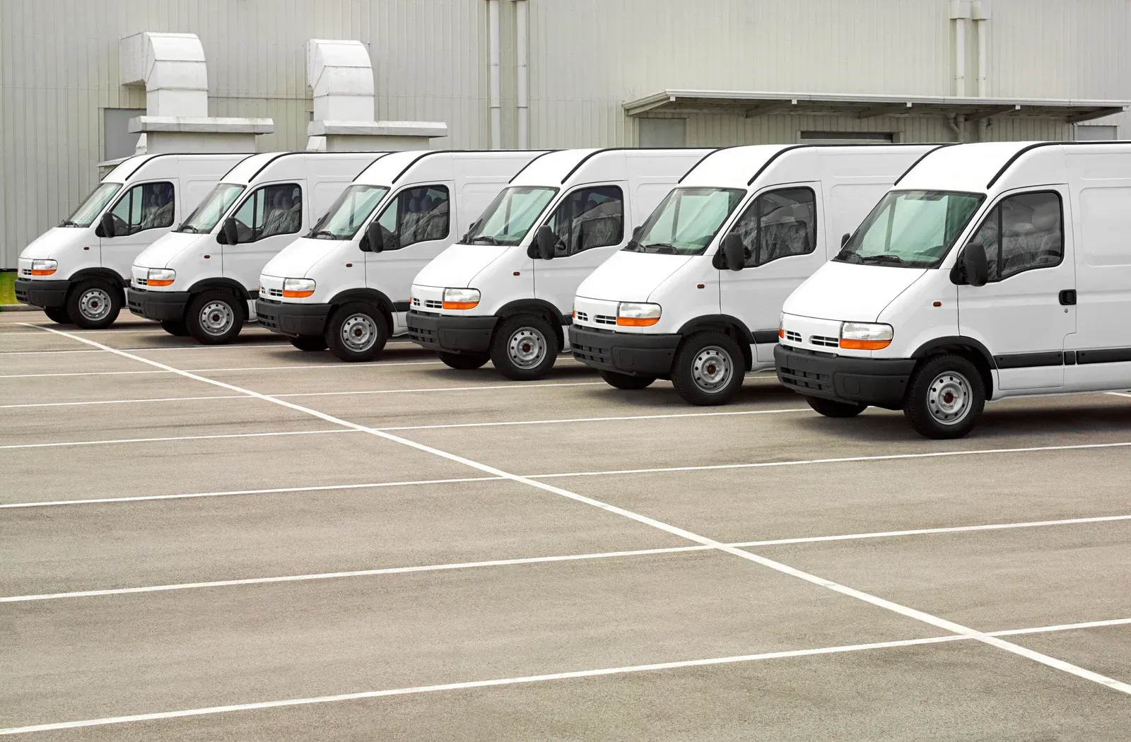 Row of white delivery vans parked in an industrial parking lot.