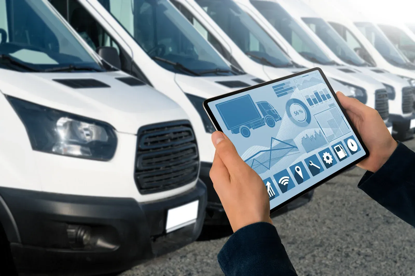 Person holding a tablet with data, looking at a row of white delivery vans.