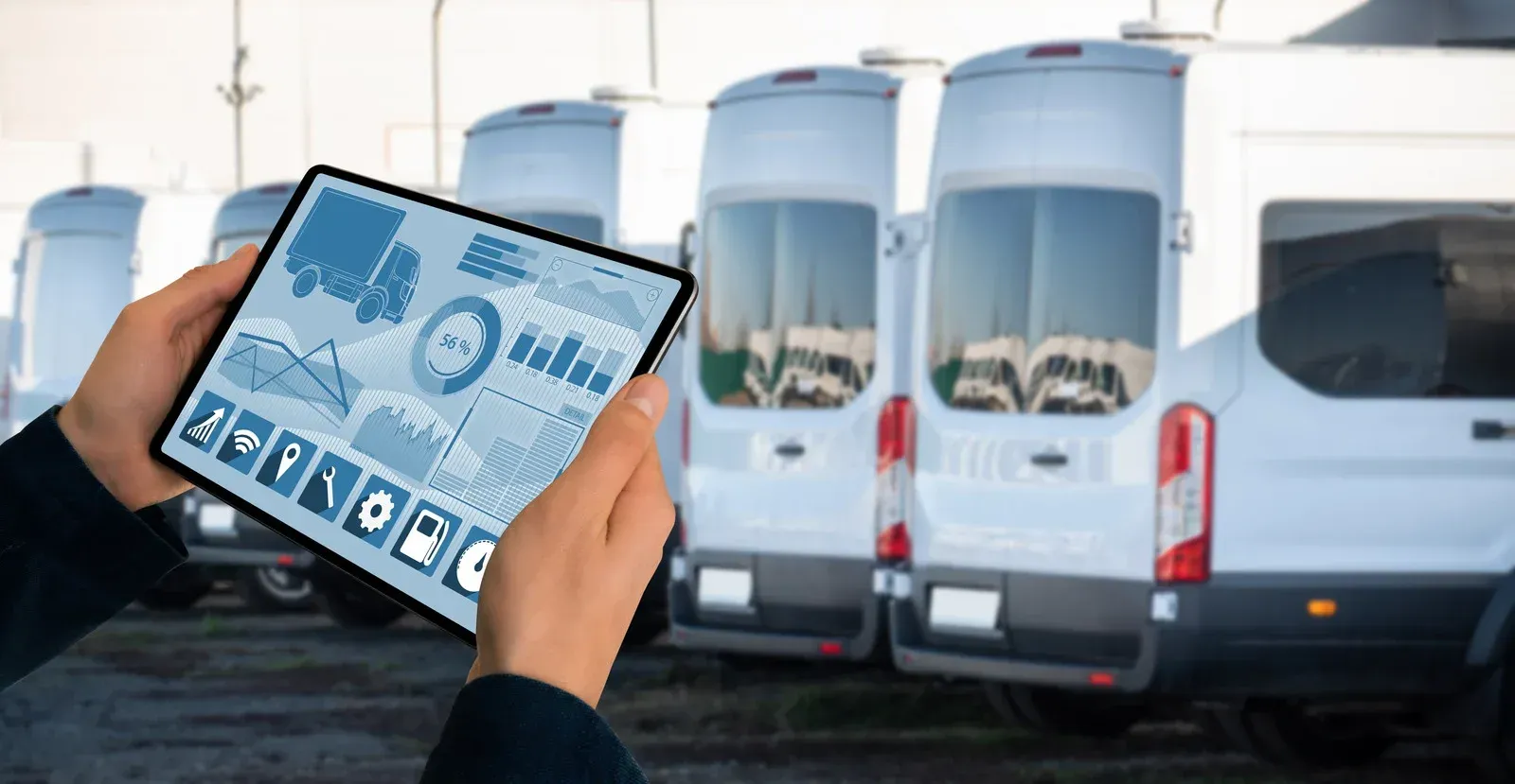 Person holding tablet displaying fleet management data in front of a row of white vans.