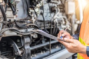 Mechanic in safety vest inspects fleet vehicle engine, writing on clipboard in sunlight.