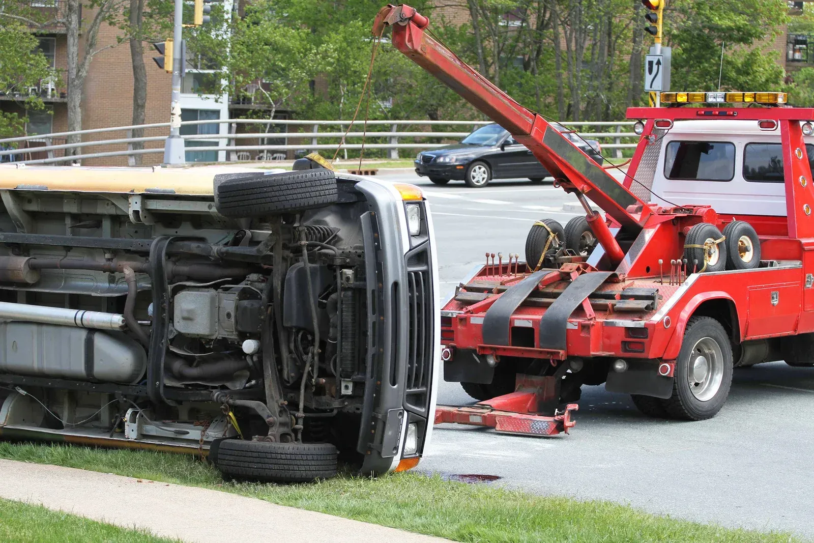 A red tow truck lifting a flipped white van at an intersection with a green lawn.