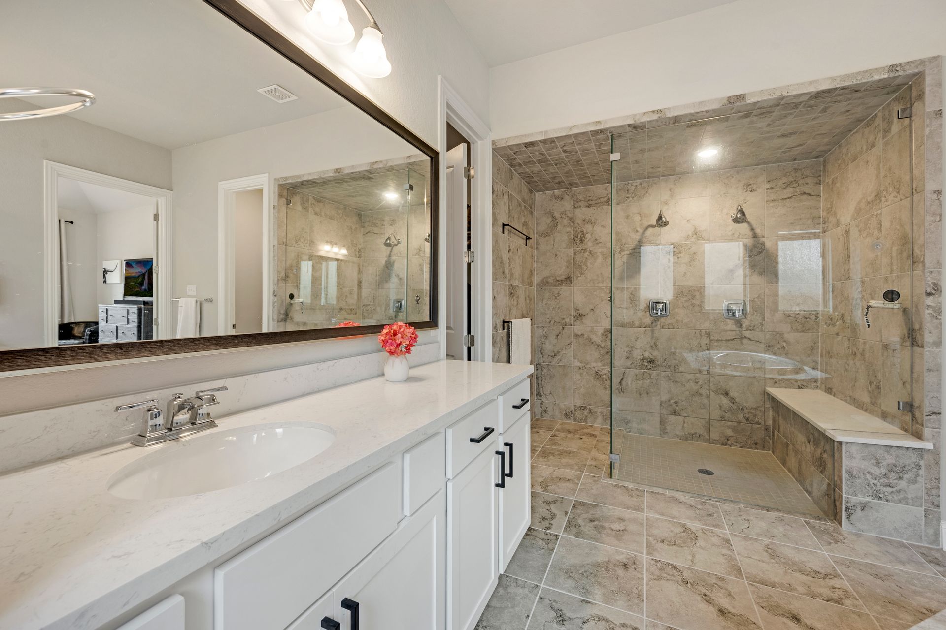 A modern bathroom featuring a white vanity with a marble countertop, a large mirror, and a spacious walk-in stone shower.