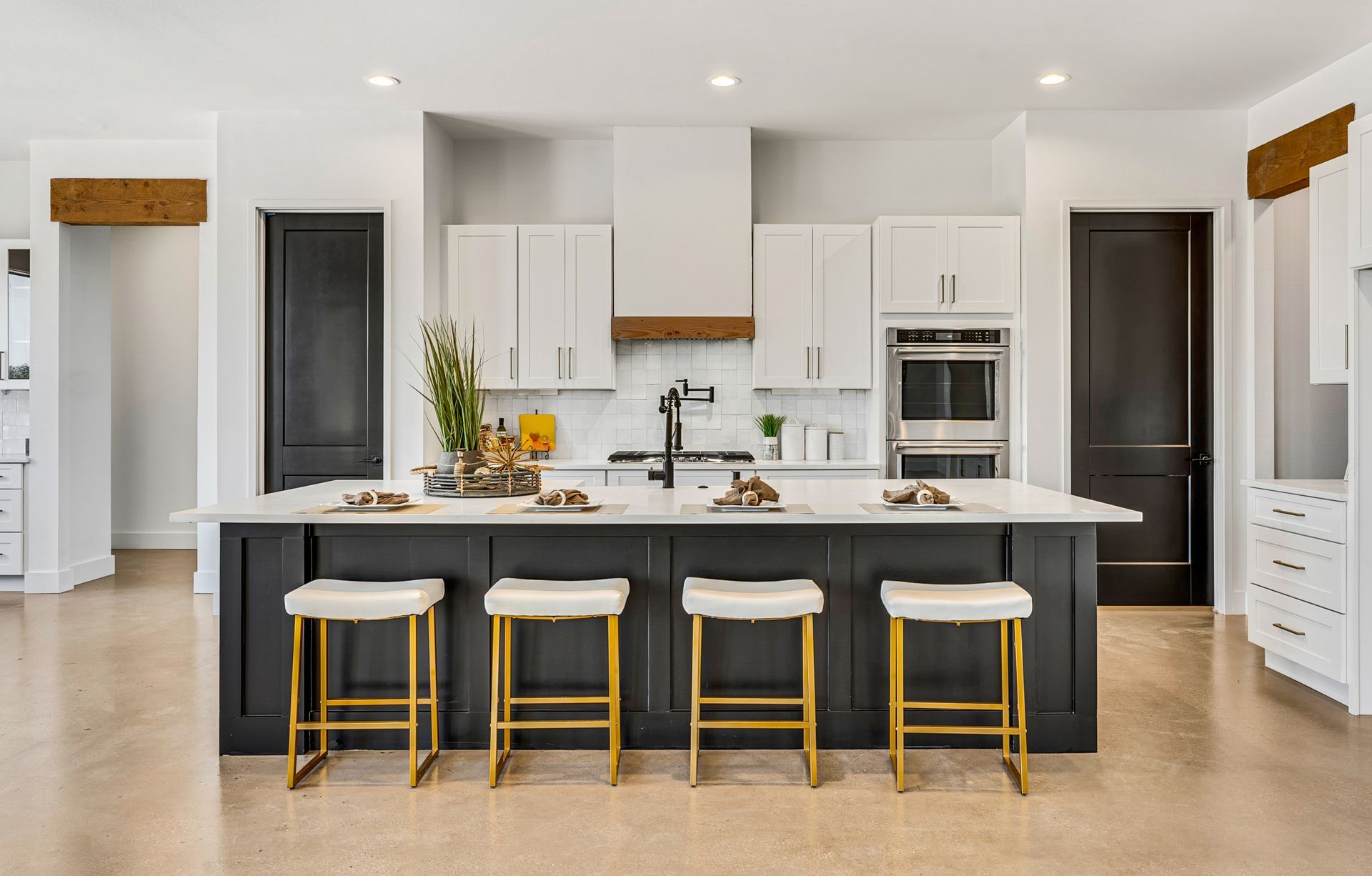 A modern kitchen featuring a dark gray island with four bar stools, white upper cabinets, and a white range hood.