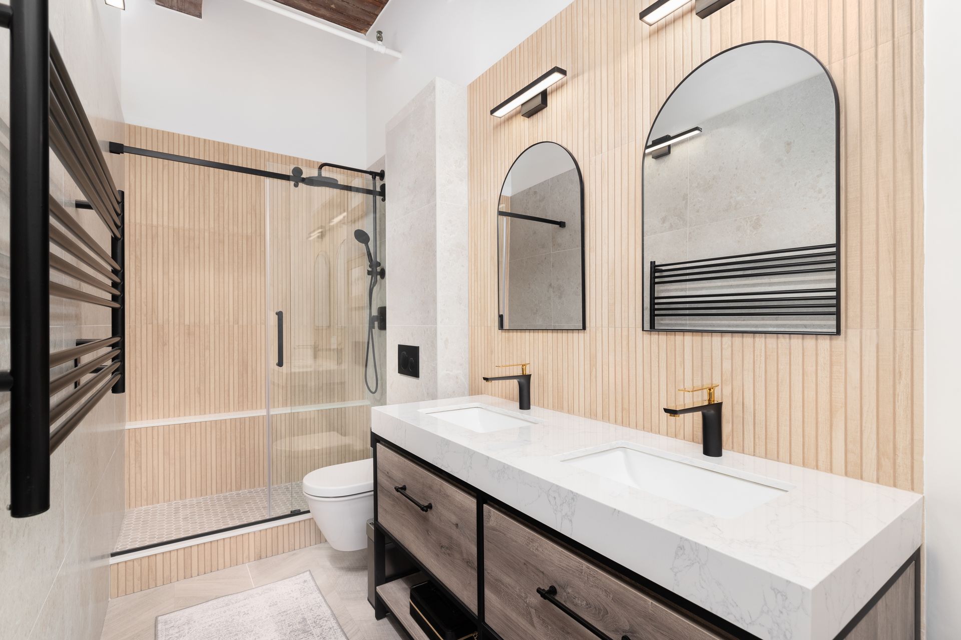 Modern bathroom with wood-slat walls, double vanity, matte black fixtures, arched mirrors, and a glass-enclosed shower.
