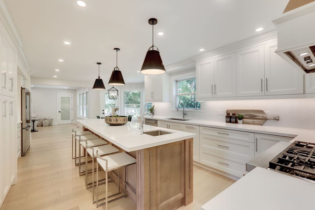 A bright modern kitchen with a wooden island, white cabinets, white countertops, and three hanging black pendant lights.