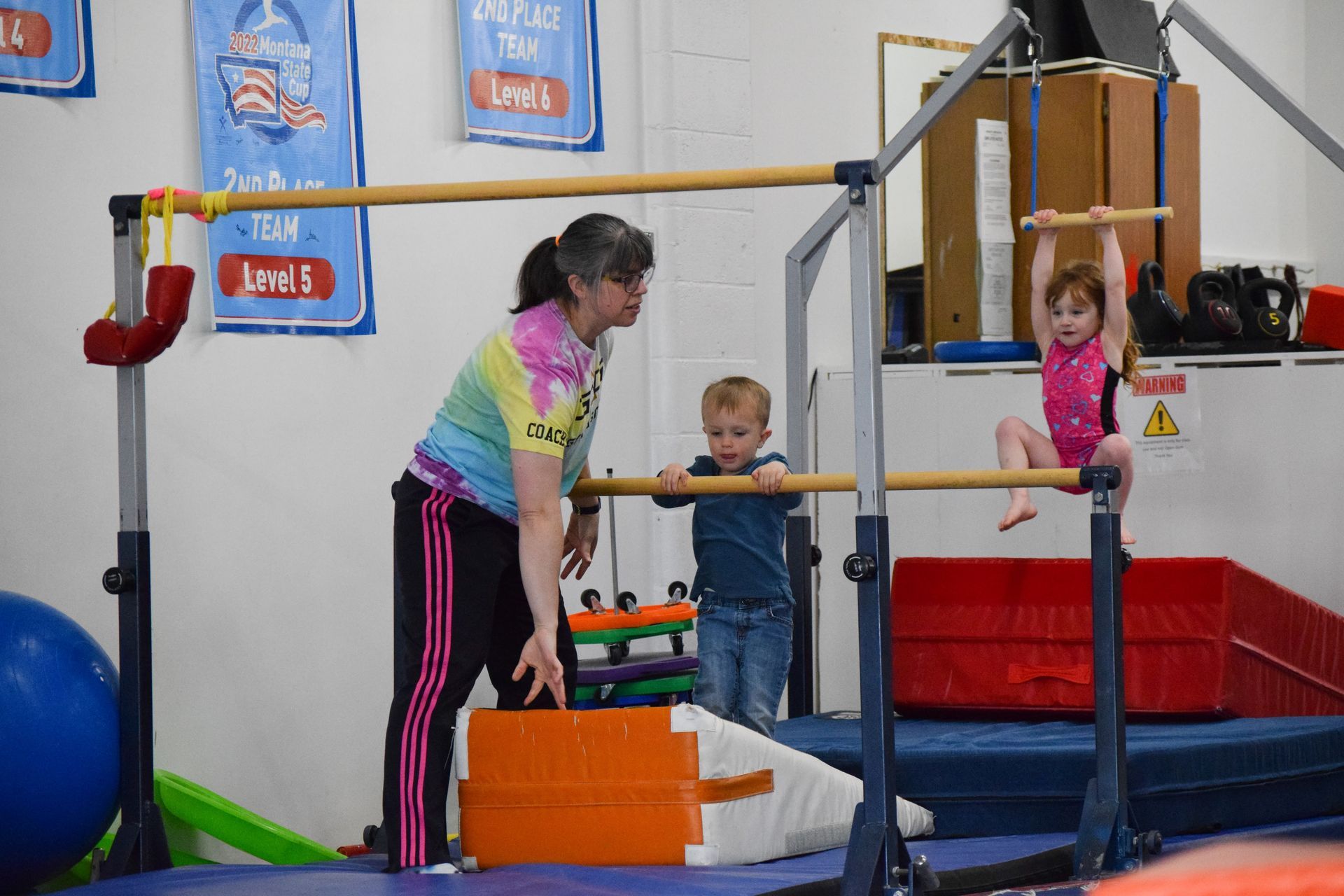 A woman is helping two young children do exercises on a gymnastics bar.