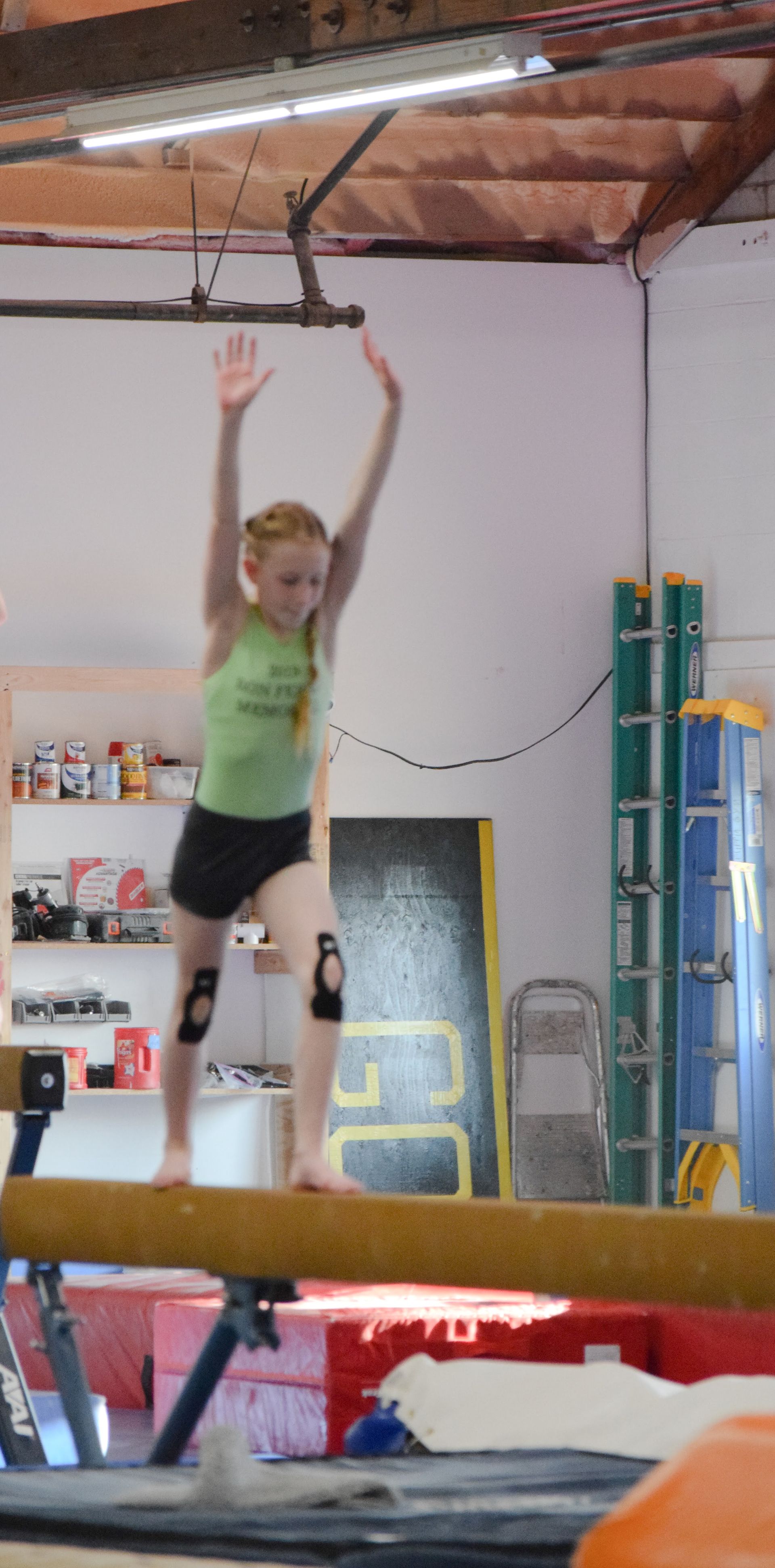 A young girl is standing on a balance beam in a gym.