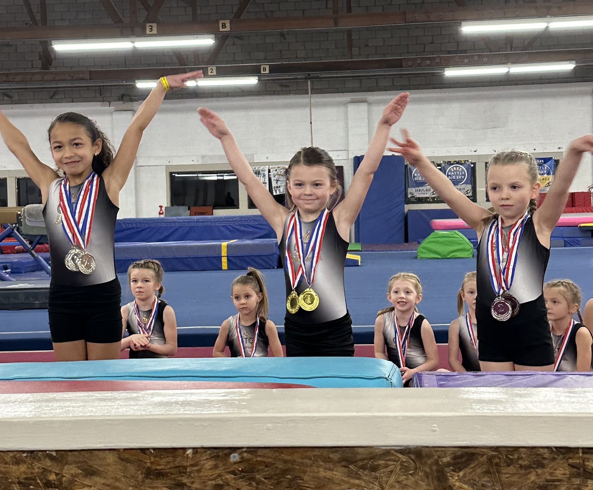 A group of young girls are wearing medals and raising their arms in the air