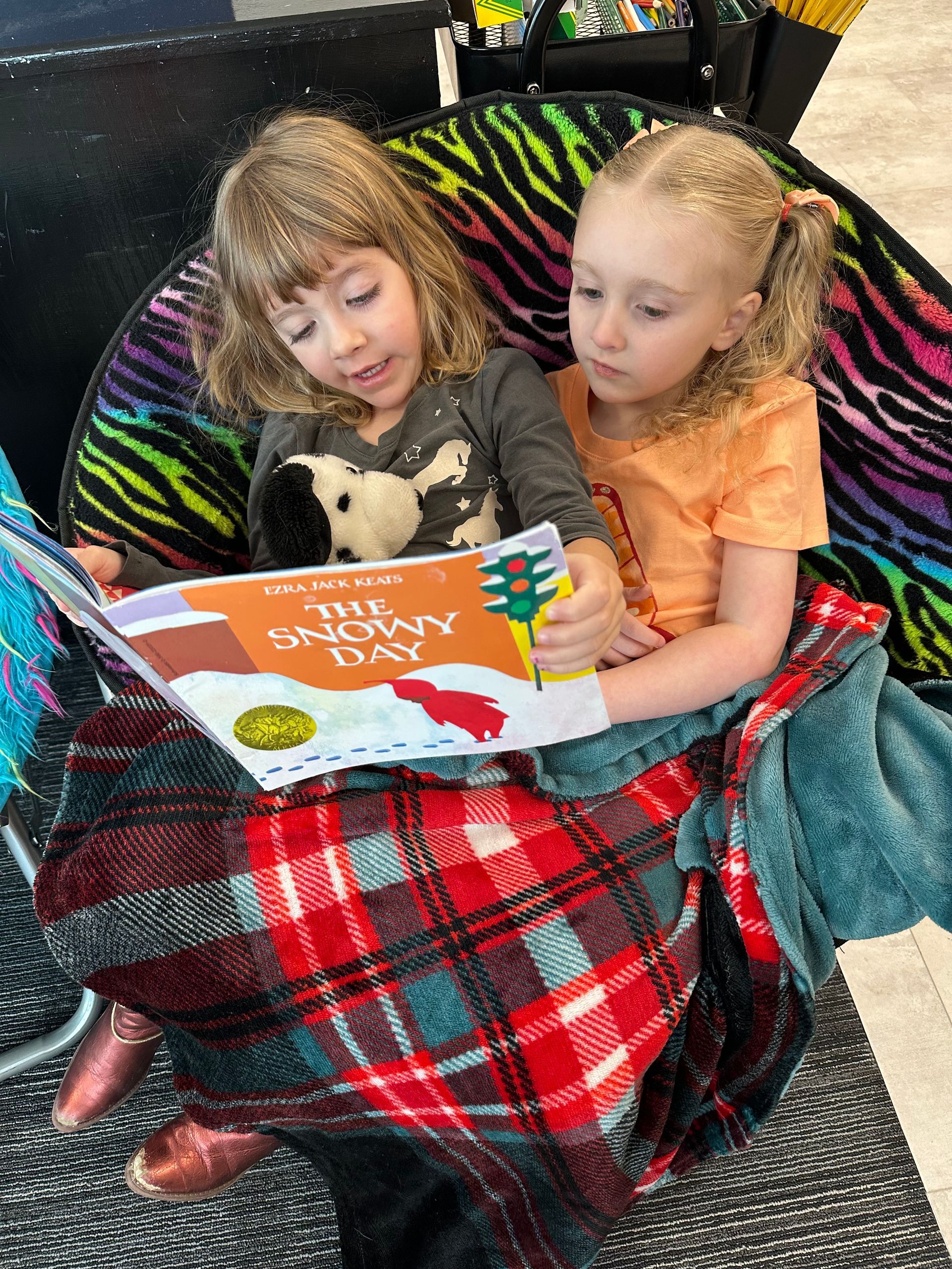 A boy and a girl are laying on the floor reading a book.