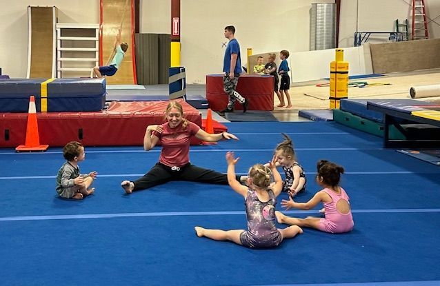 A woman is helping two young children do exercises on a gymnastics bar.