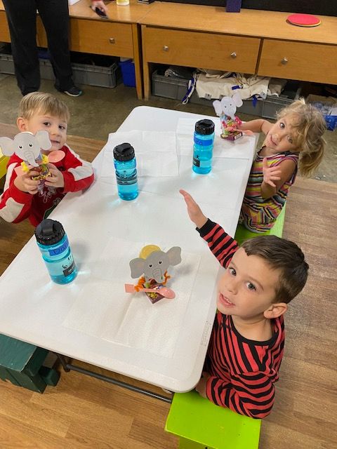 Three children are sitting at a table with water bottles and elephants on it.
