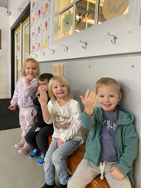 A group of children are sitting on a bench in a hallway.