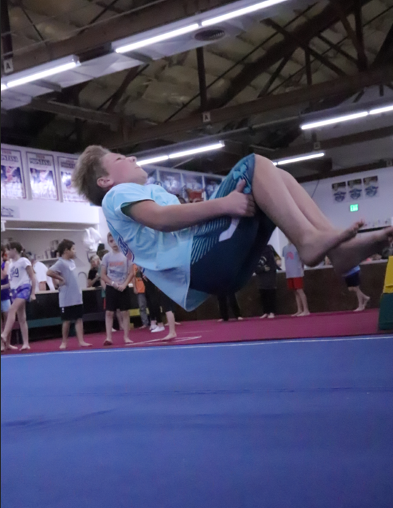 A young boy is doing a flip on a blue mat