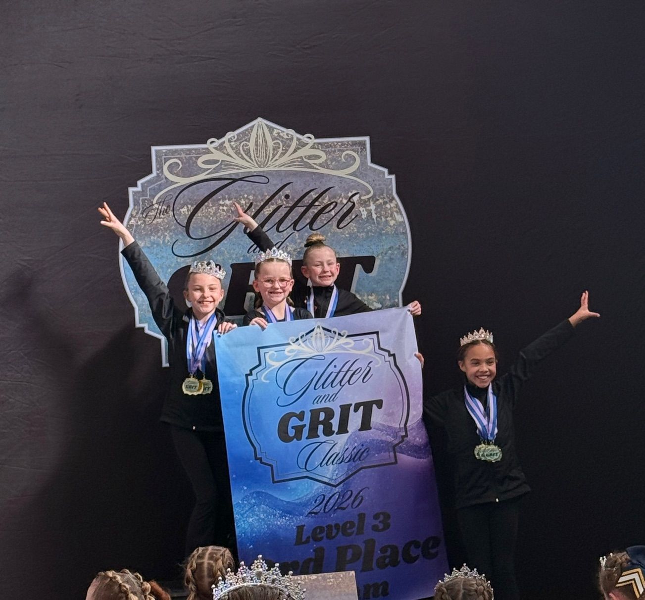 A group of young girls are wearing medals and raising their arms in the air