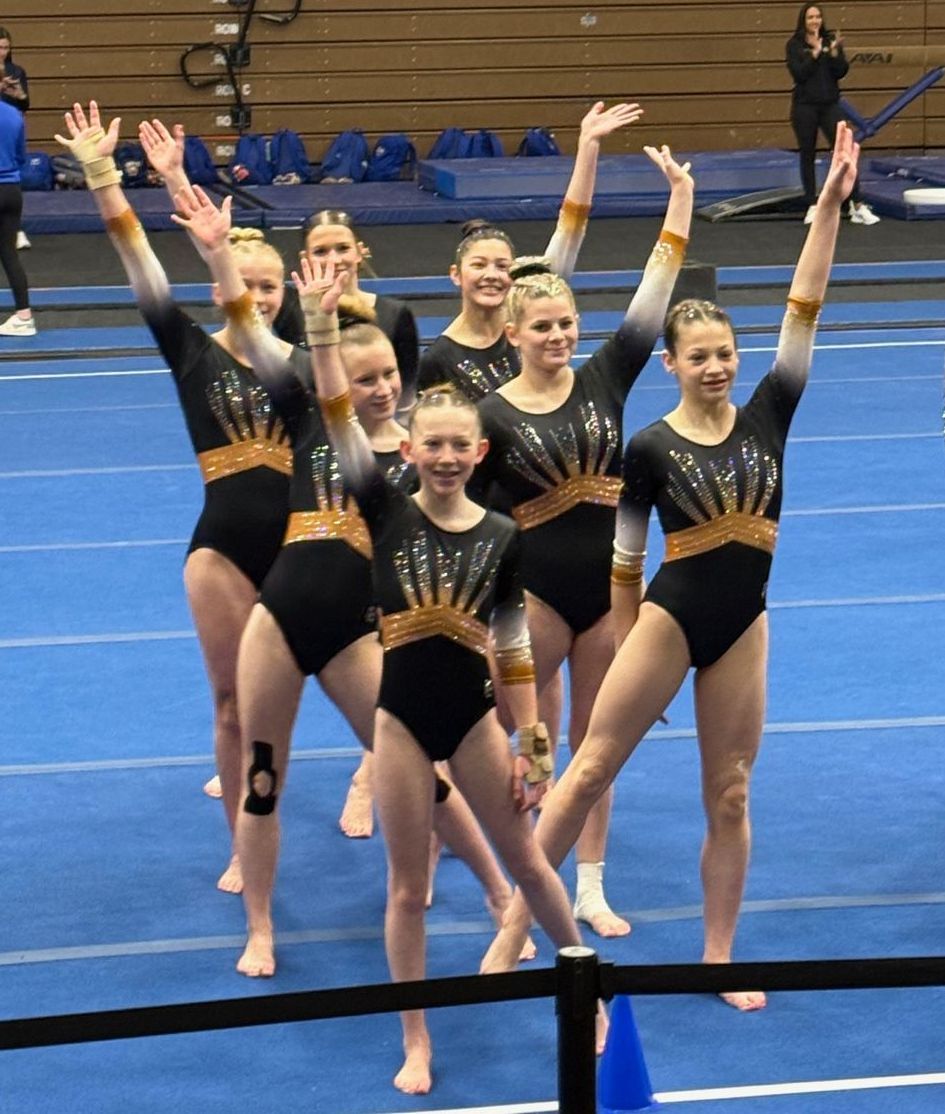 A group of young girls are sitting on a balance beam in a gym.