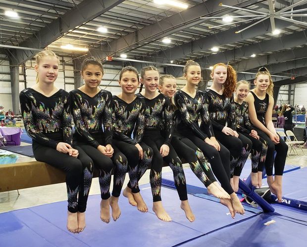 A group of young girls are sitting on a balance beam in a gym.