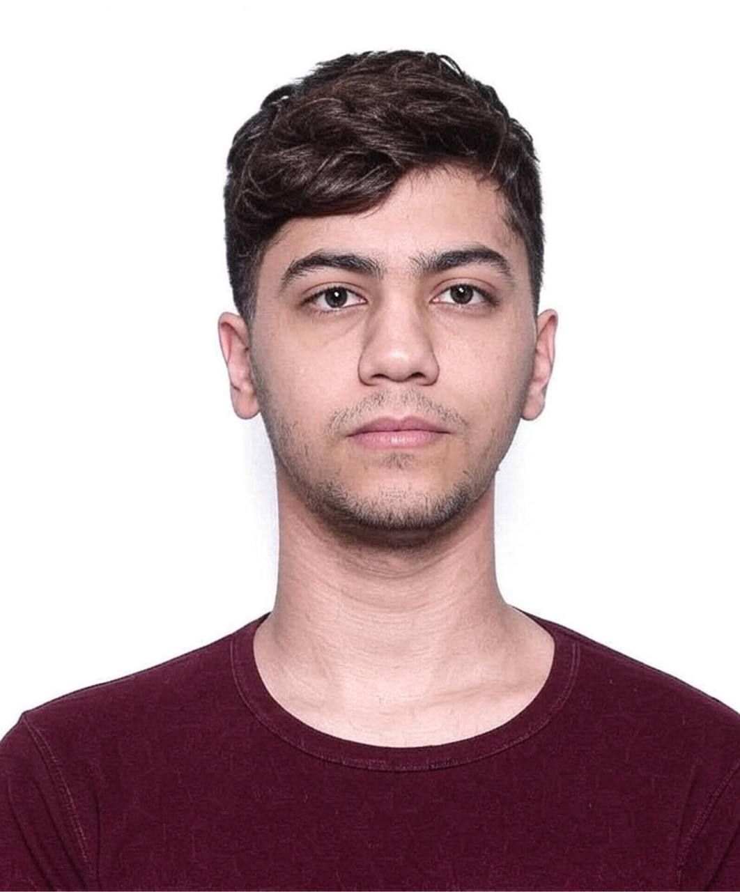 A man with a beard is wearing a black shirt and a blue jacket.