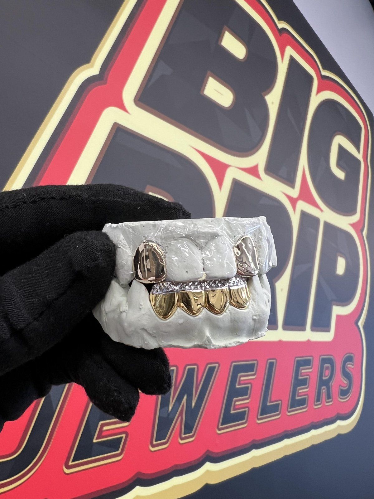 A person is holding a model of teeth in front of a big drip jewelers logo