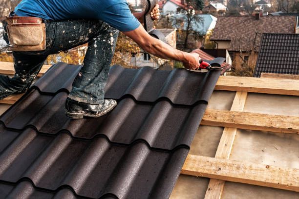 Professional roofer with blue shirt installs tiles on wooden base of roof.