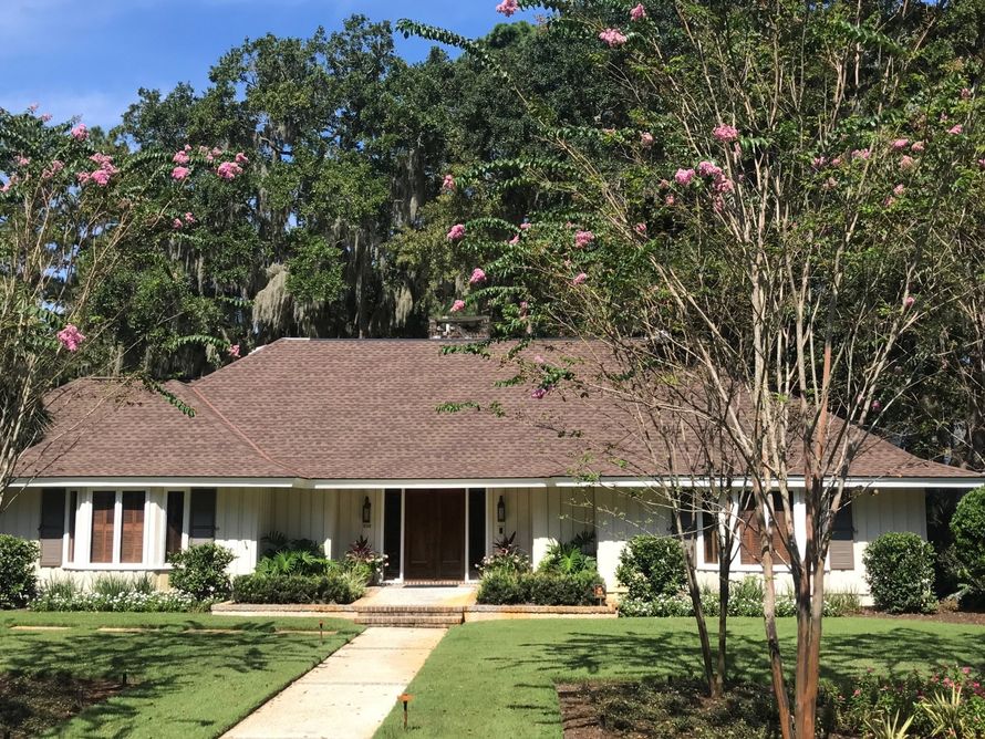 A white house with a brown roof is surrounded by trees and grass.