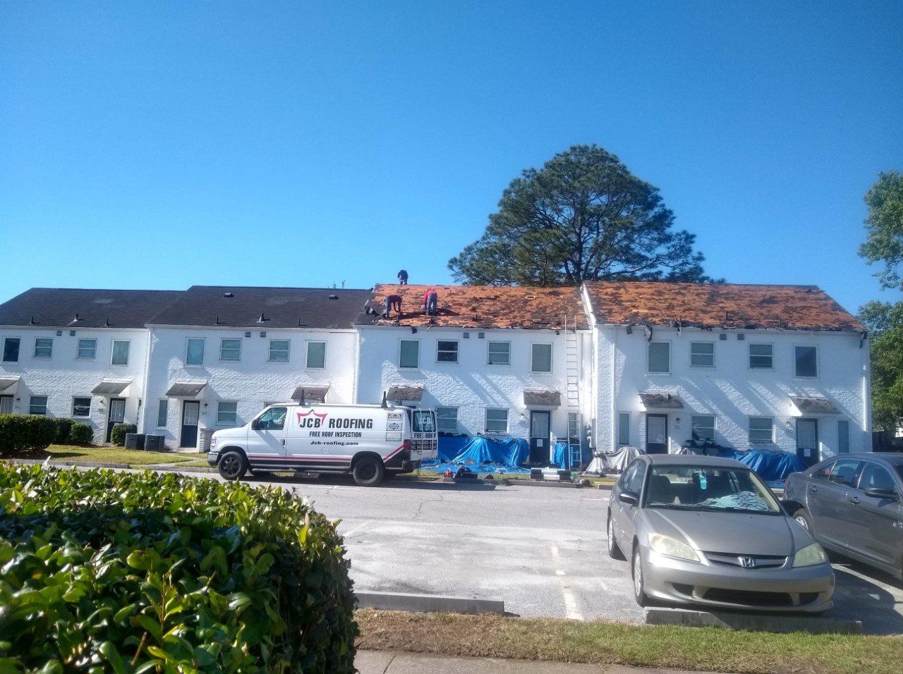 Row of townhouses with roofing being repaired; white walls, blue tarps, work truck, cars.