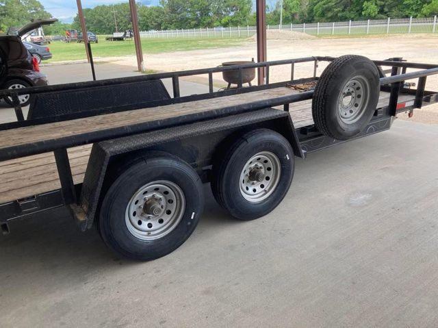 Black flatbed trailer with dual axles and spare tire under a metal shelter