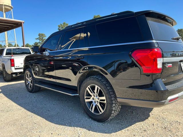 Black SUV parked on a gravel lot beside a covered structure, viewed from the rear side