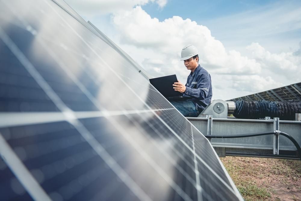 A Man Is Sitting On Top Of A Solar Panel Using A Laptop — Mission Solar And Electrical In Innisfail, QLD