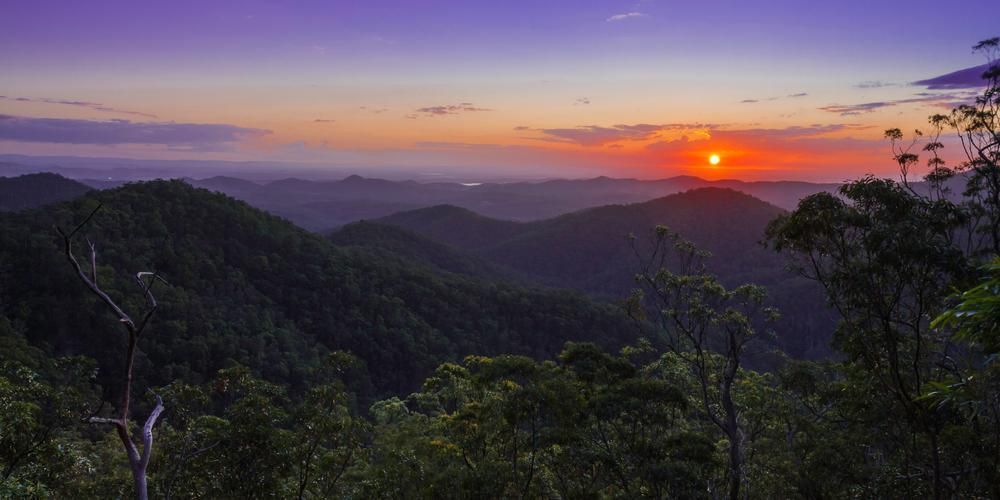 The Sun Is Setting Over A Mountain Range With Trees In The Foreground — Mission Solar And Electrical In Cardwell, QLD